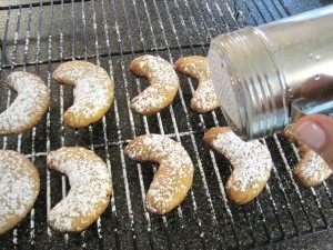 Sprinkling the Almond Crescent Cookies with powdered sugar.